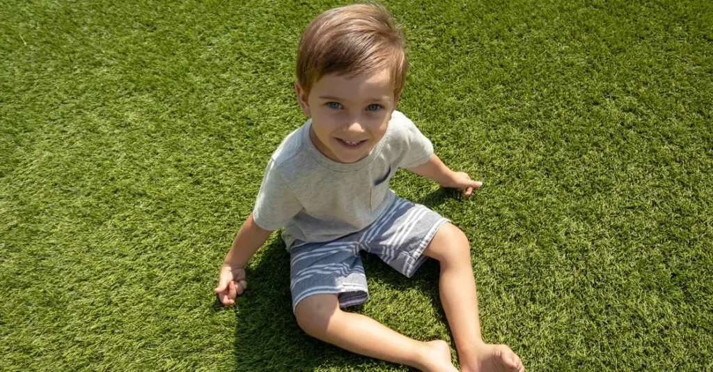 Child sitting on green grass, smiling, wearing a light shirt and shorts