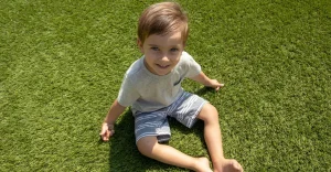 Child sitting on green grass, smiling, wearing a light shirt and shorts