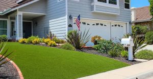 A gray house with a garden, mailbox, and American flag in front yard