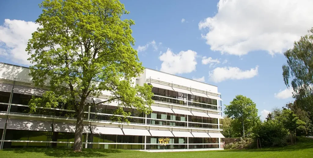 Modern building with large windows, surrounded by green trees and a clear blue sky