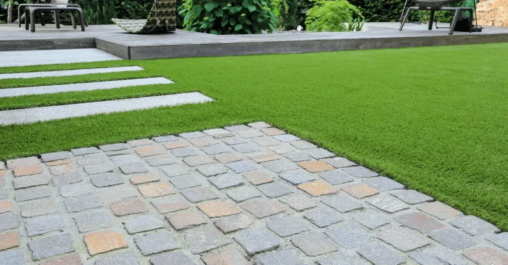 A garden scene with green grass, stone walkway, and a patio in the background