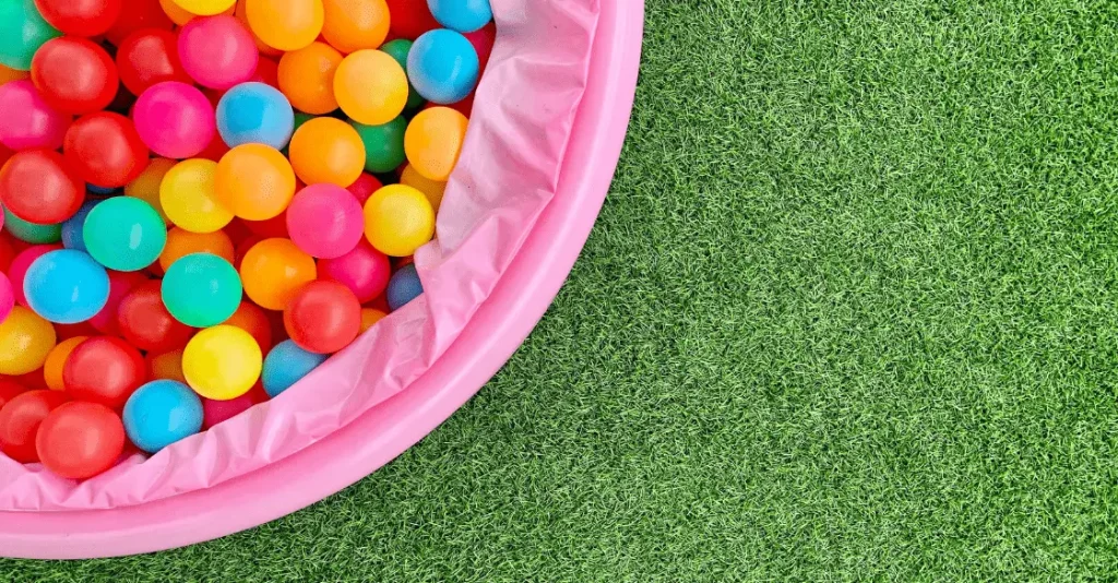 A pink ball pit filled with colorful plastic balls on green grass