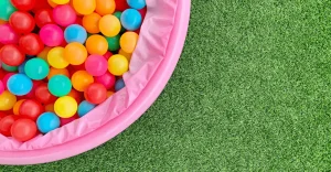 A pink ball pit filled with colorful plastic balls on green grass