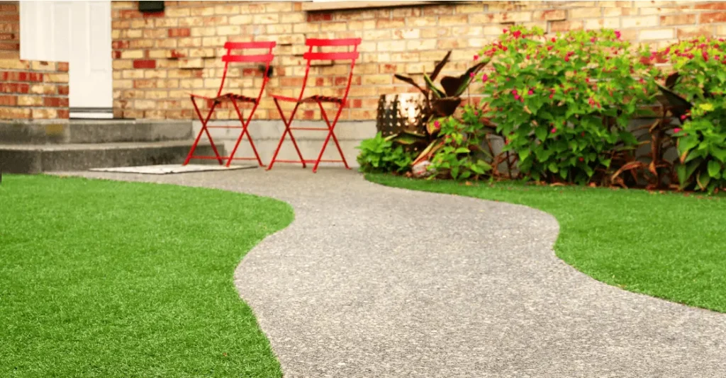 A curved stone pathway leads to two red chairs near a brick wall and greenery