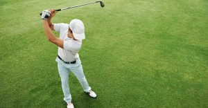 Person in a white cap swings a golf club on a green field