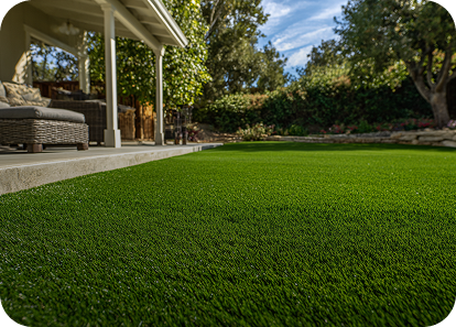 Green artificial turf in a backyard with a patio and trees in the background