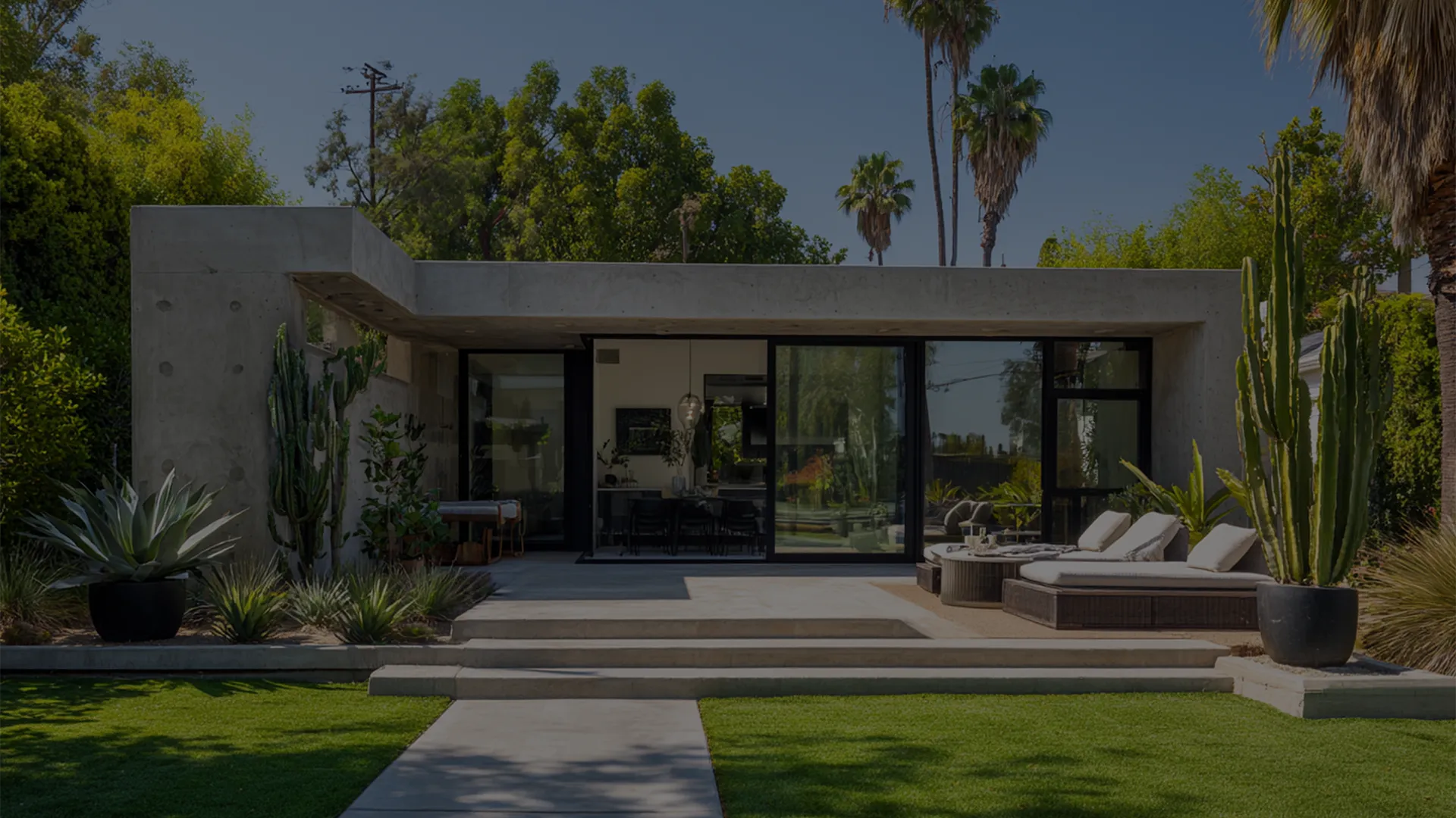 Modern house with large windows, surrounded by greenery and palm trees