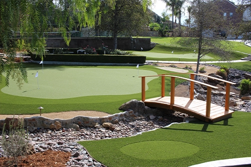 Landscape featuring putting greens, a wooden bridge, and stone pathways among greenery