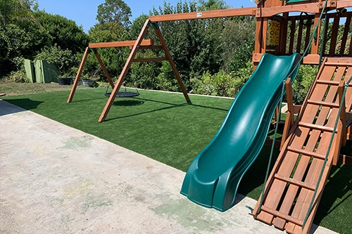 Playground with a green slide, swings, and a climbing frame on artificial grass