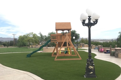 Wooden playground structure with a slide on grass, lamp post nearby, and park scenery