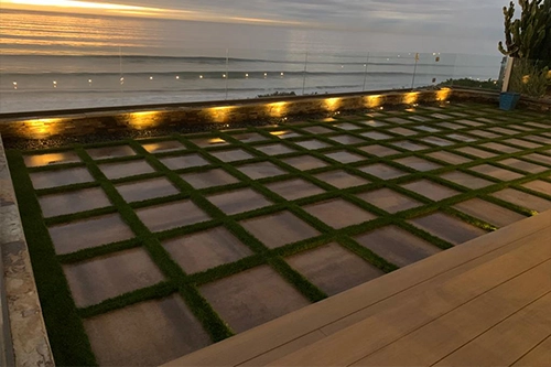 Patio with a grid pattern of grass and stone slabs, ocean in the background at sunset