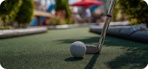 Close-up of a golf club and a white golf ball on a green putting surface