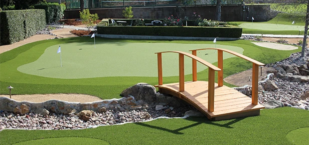 A wooden bridge over rocks in a green lawn area with a putting green