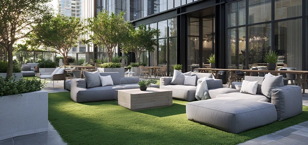 Outdoor lounge area with gray seating, tables, and greenery. Modern building in background