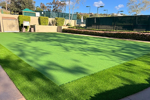 Green artificial turf with surrounding plants and a fenced area in the background