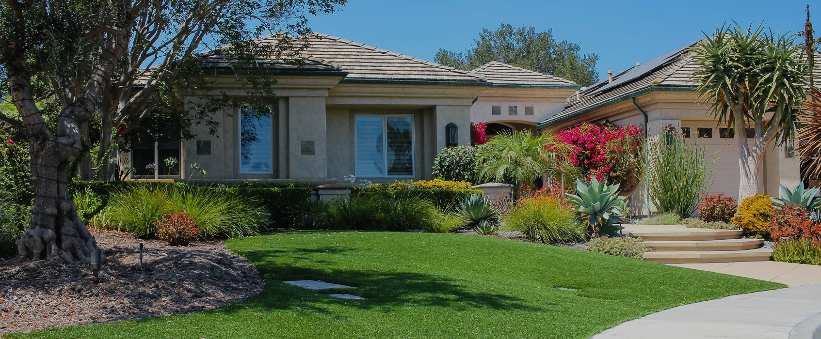 A suburban house with landscaping, flowers, and a green lawn under a clear blue sky