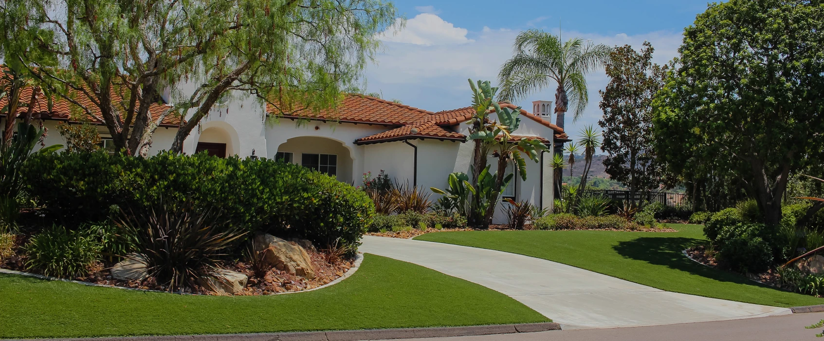 A house with a tiled roof, surrounded by green grass and tropical plants