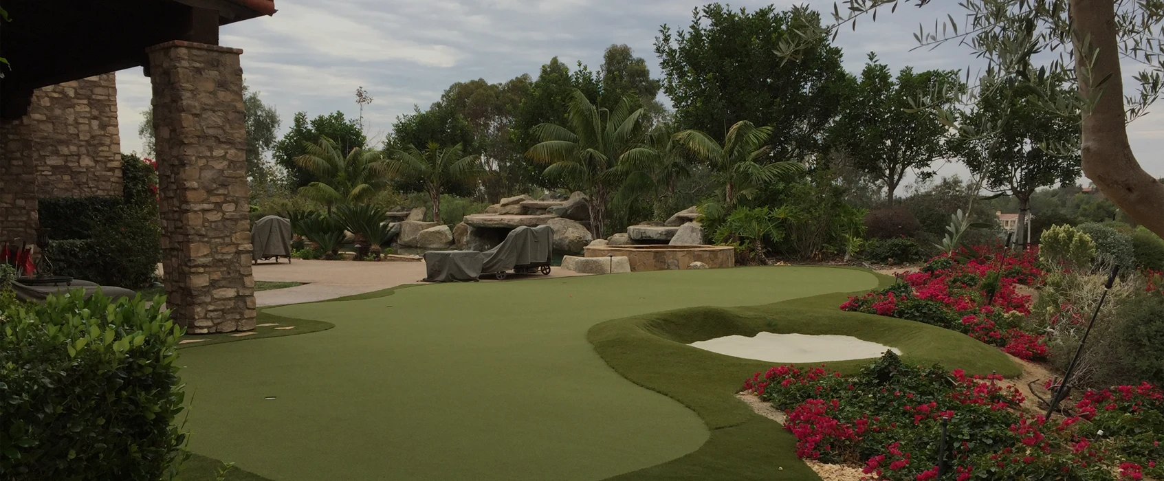 Green golf course area with rocks, palm trees, and flower beds under a cloudy sky