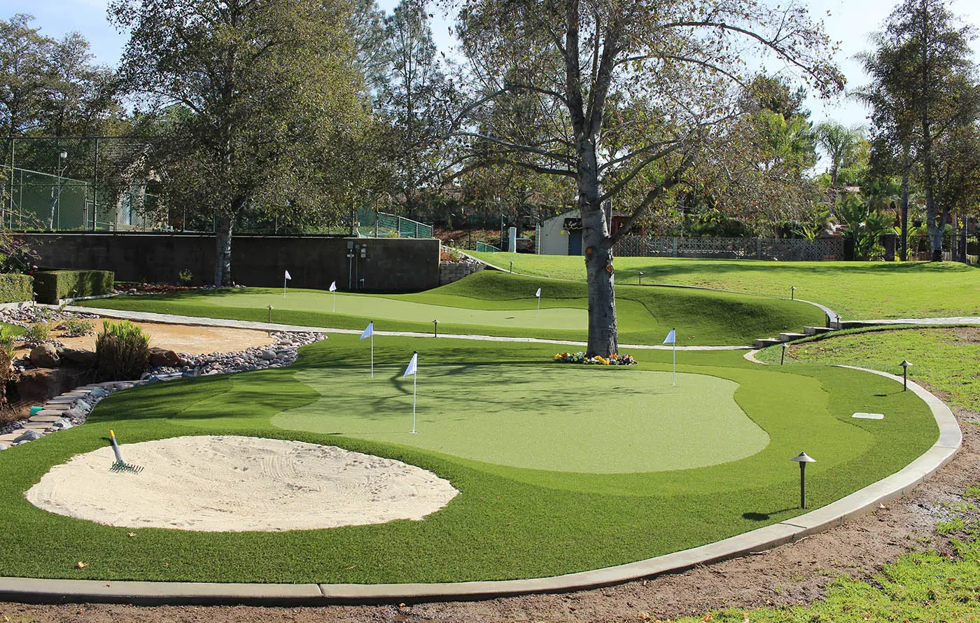 A golf putting green with a sand trap, trees, and flags on the green surface