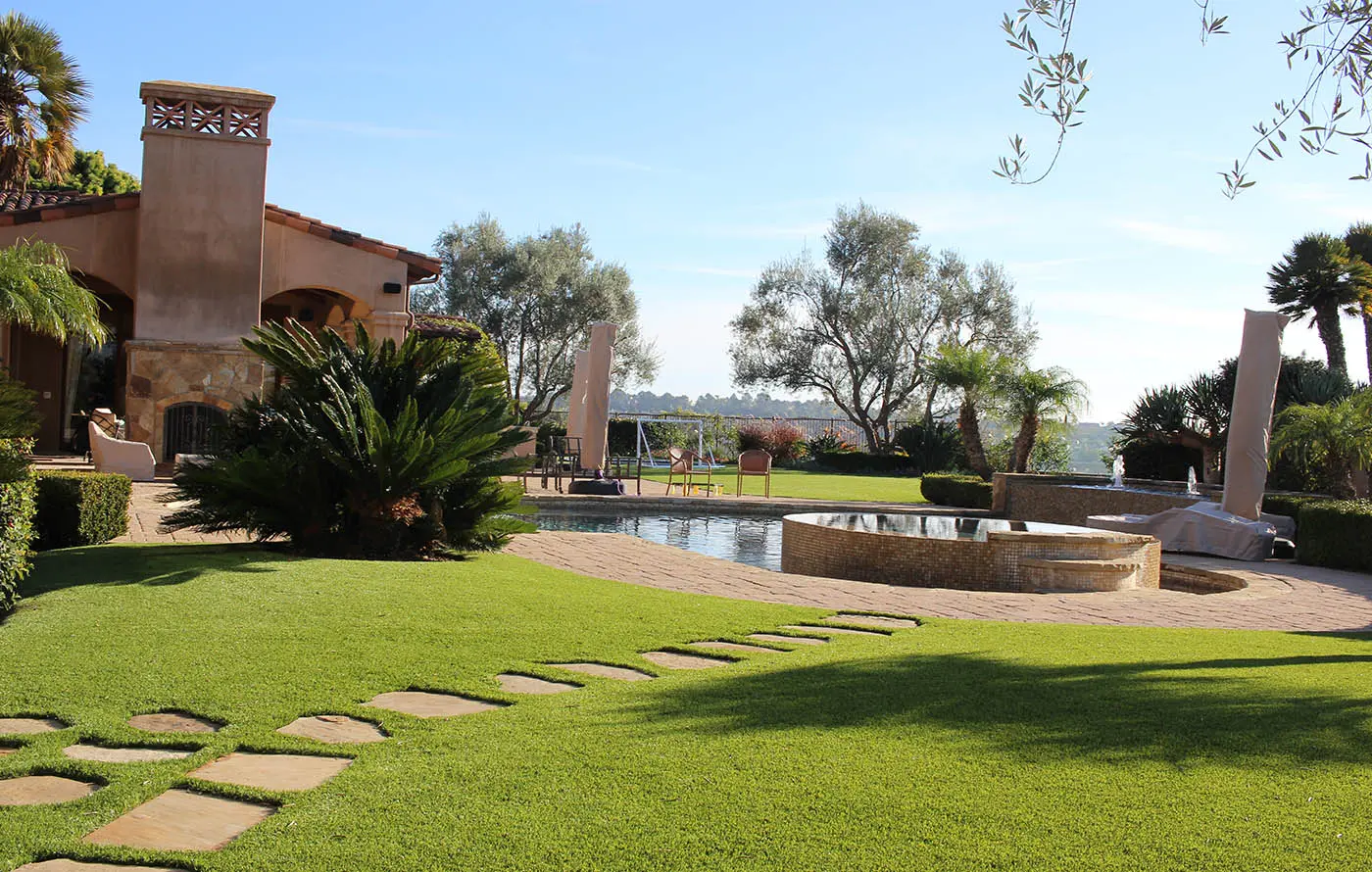 View of a spacious garden with a pool, stone pathway, and greenery