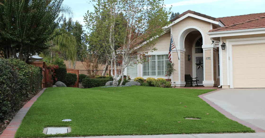 A house with a manicured lawn, trees, and an American flag. Garage is on the right