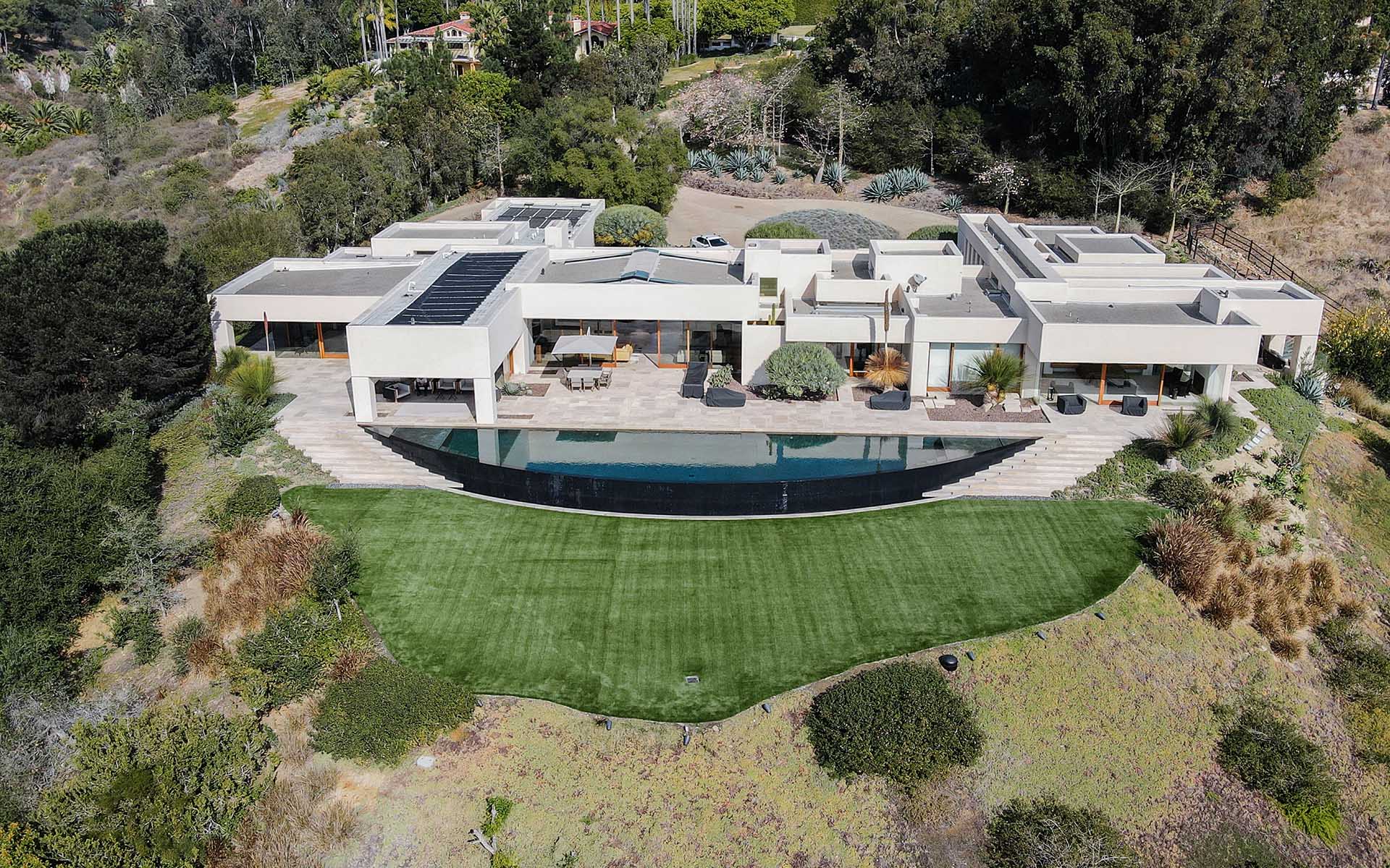Aerial view of a modern, single-story house with a pool and lawn