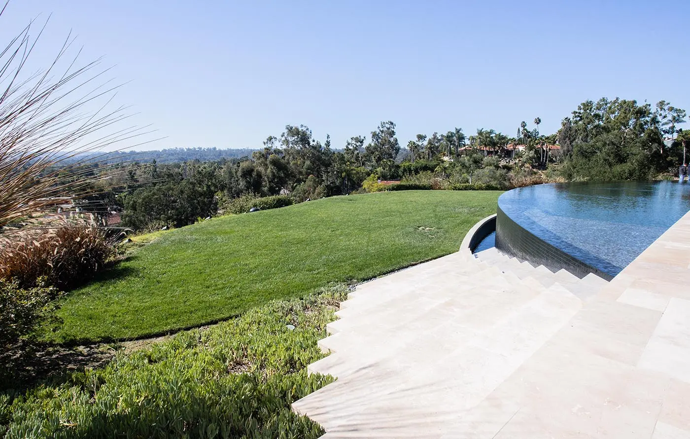 A landscaped yard with a swimming pool and lush greenery under a clear blue sky