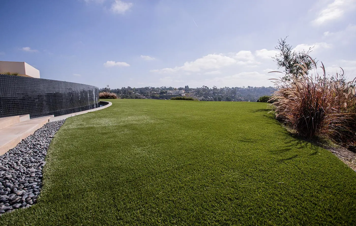 Green lawn with stone border, low shrubs, and distant hills under a blue sky