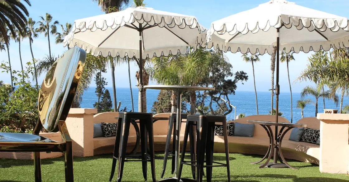 Outdoor seating area with tables, stools, and umbrellas near the ocean