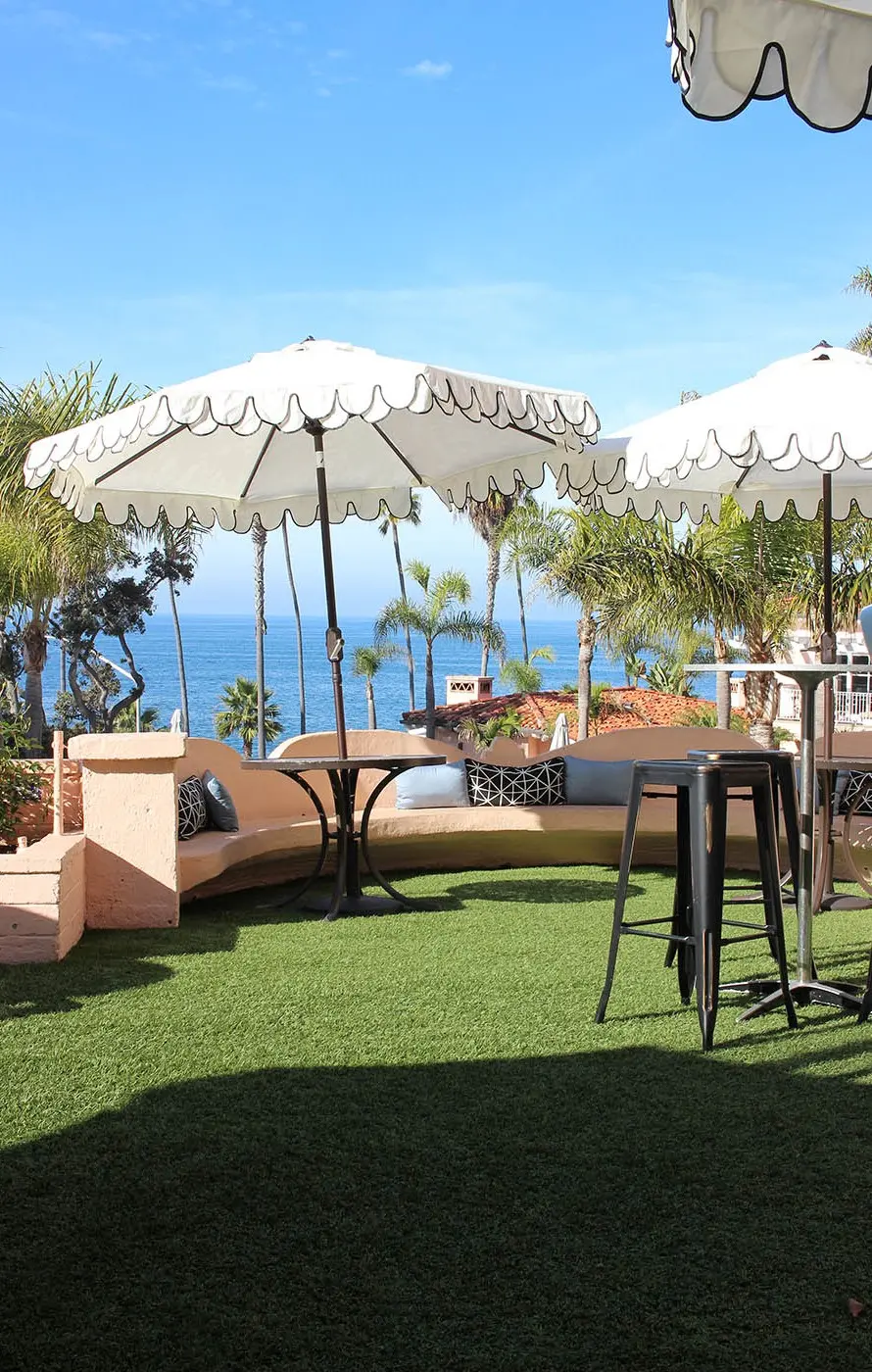 Outdoor seating area with umbrellas overlooking the ocean and green grass
