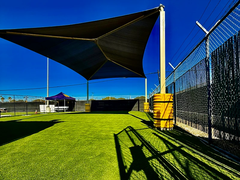 Shade structure over green grass field with a fence and blue sky