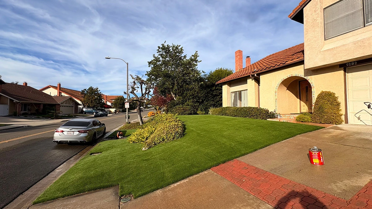 A house with landscaped lawn, parked car, and street view under a blue sky