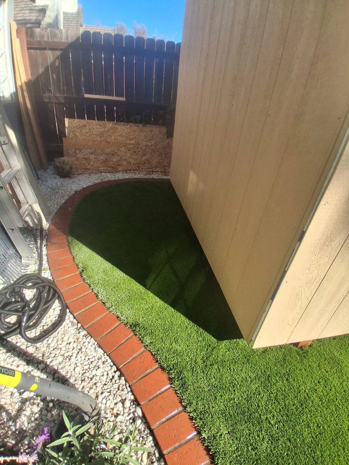 Pathway with brick border alongside a wall and artificial grass