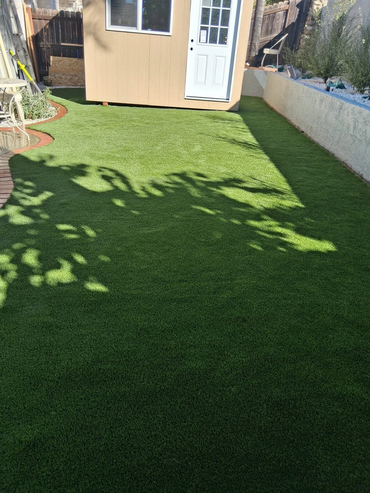Green artificial grass with a small building and shadows in a backyard setting