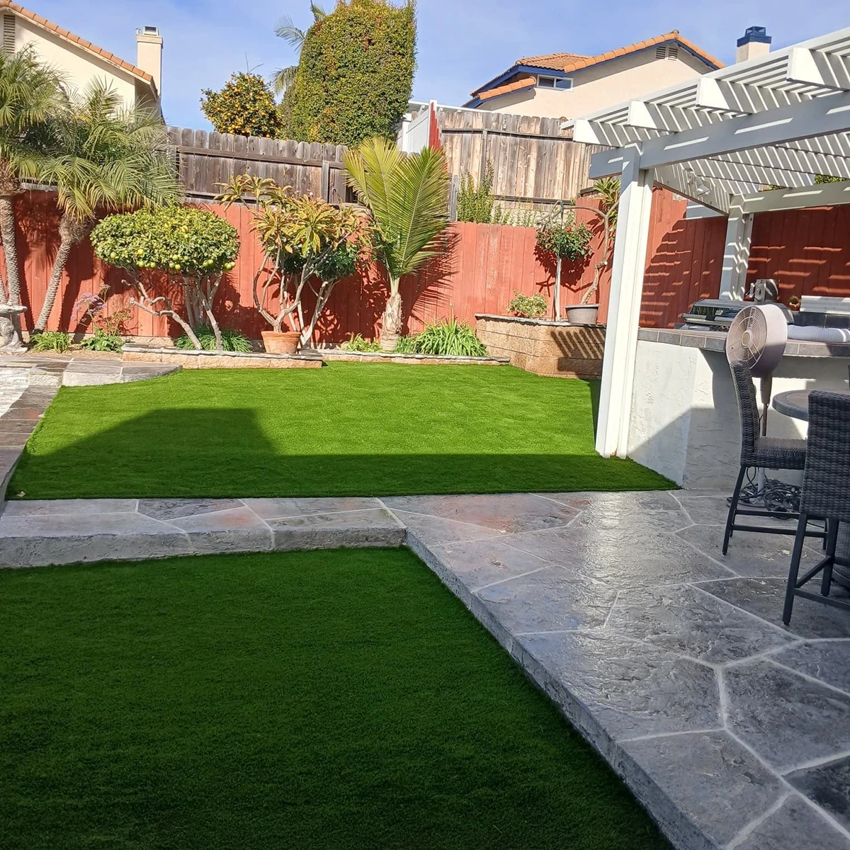 Lush green lawn with stone patio and planters, surrounded by wooden fence and trees
