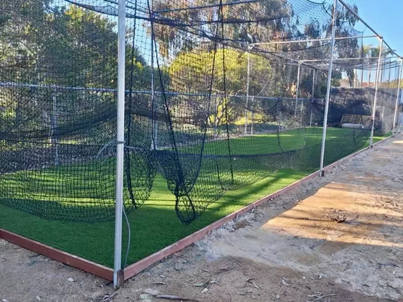 Baseball practice area with netting and artificial turf, surrounded by a fence
