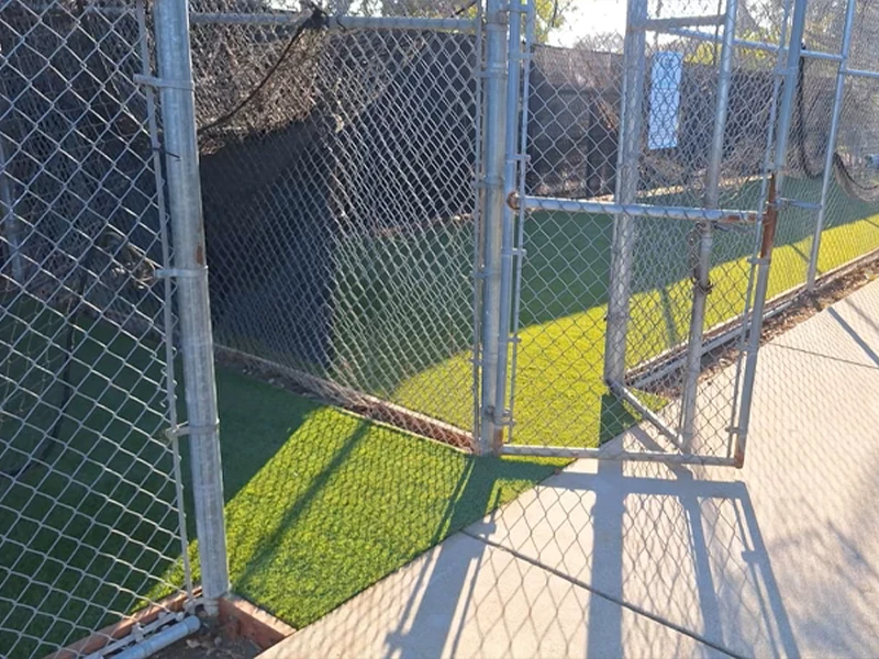 A fenced area with an open gate and artificial grass surface