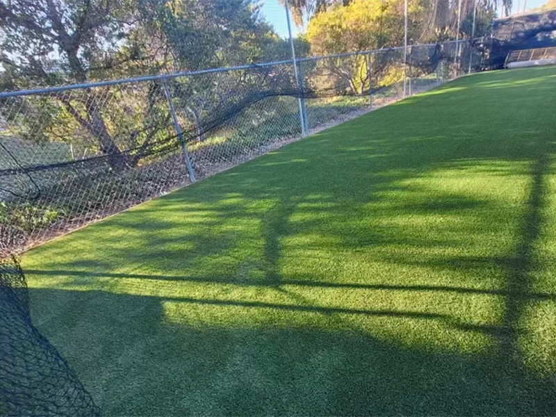 Artificial grass field bordered by a chain-link fence and trees in the background