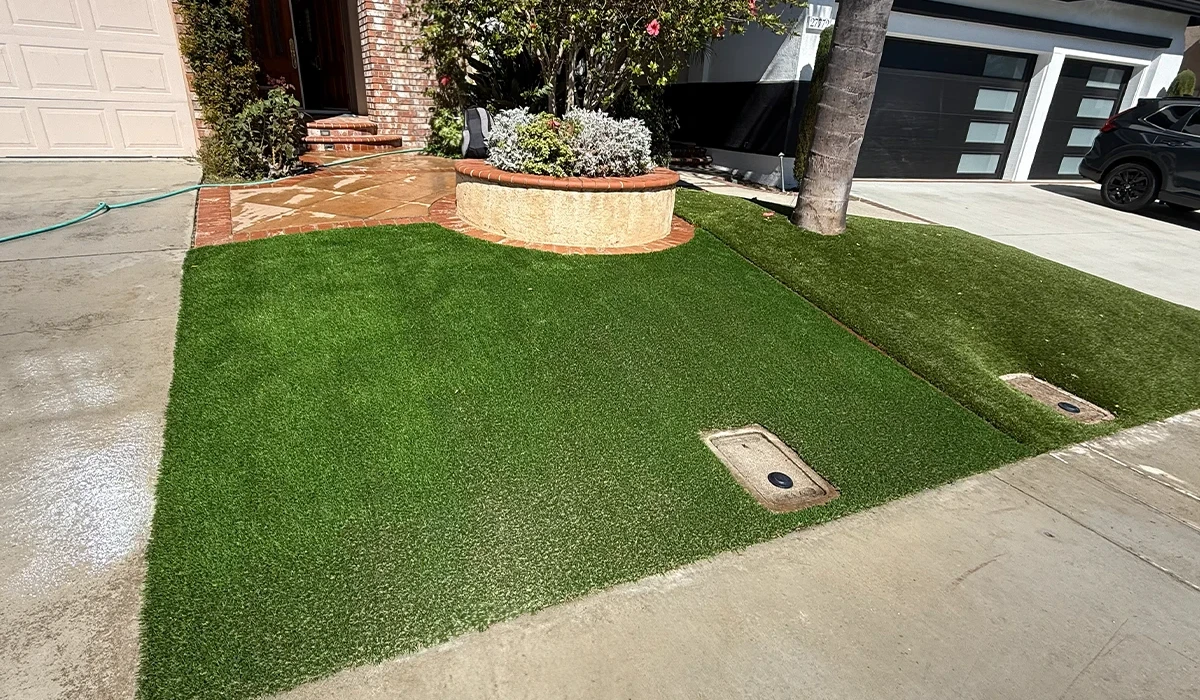 Artificial grass lawn with two drainage vents and a small landscaped area near a house