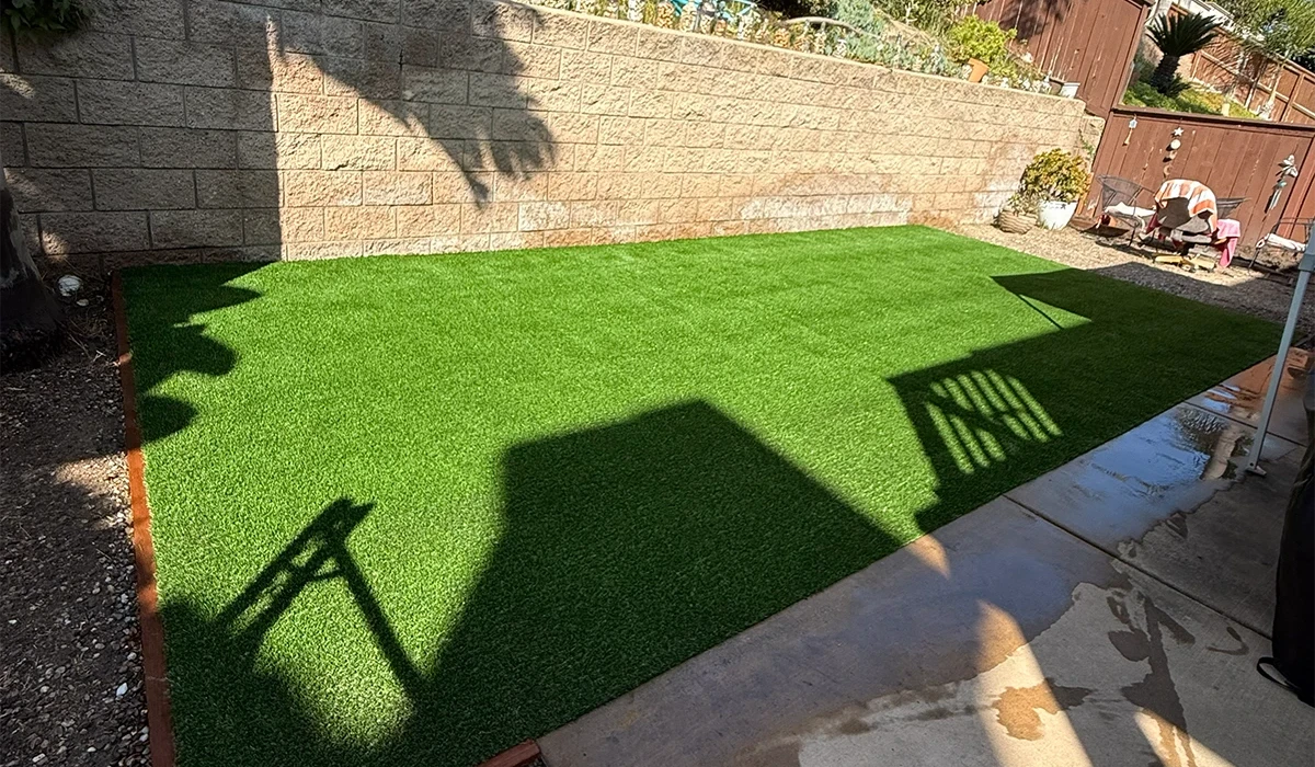 A backyard with artificial grass and a stone wall in the background