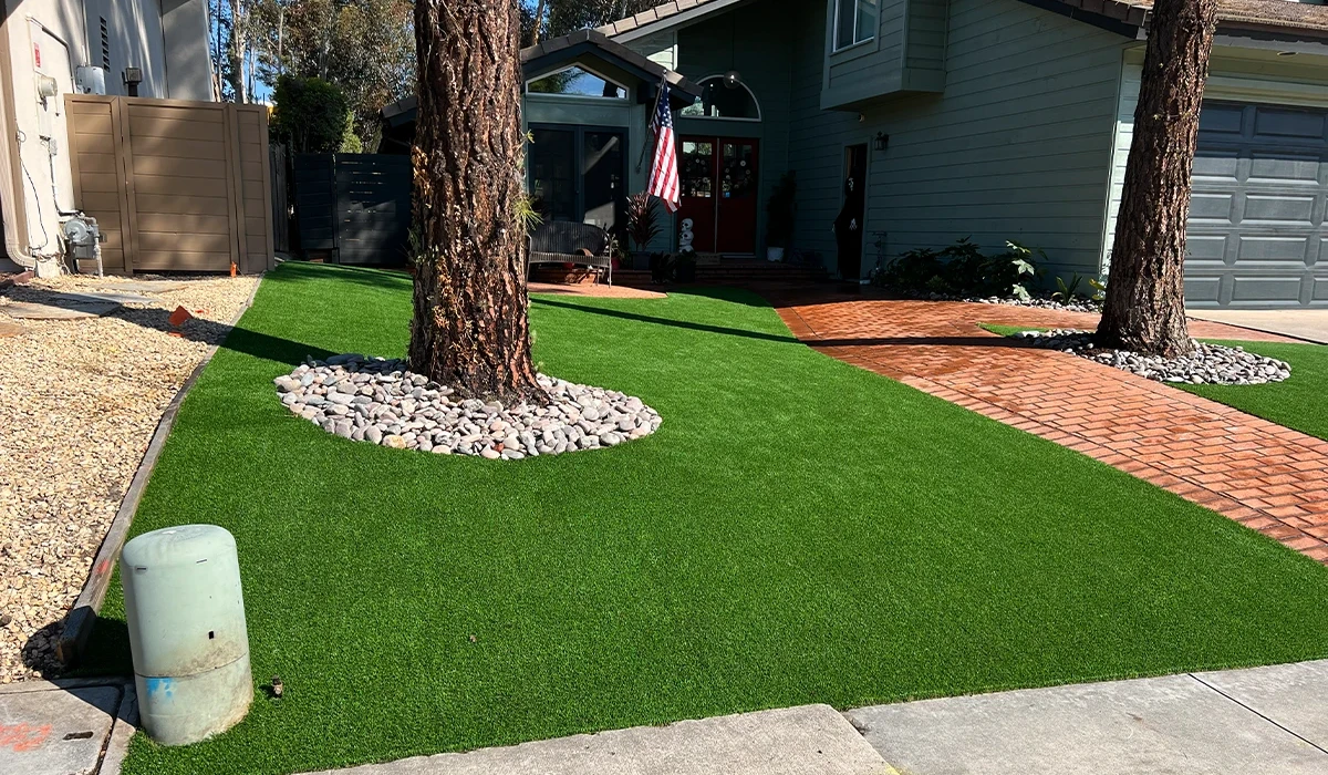 View of a yard with artificial grass, trees, and a brick pathway