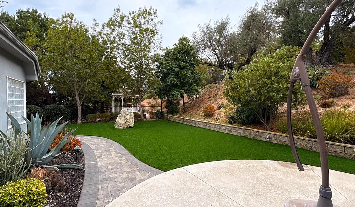 Garden view with grass, trees, a stone path, and a gazebo in the background