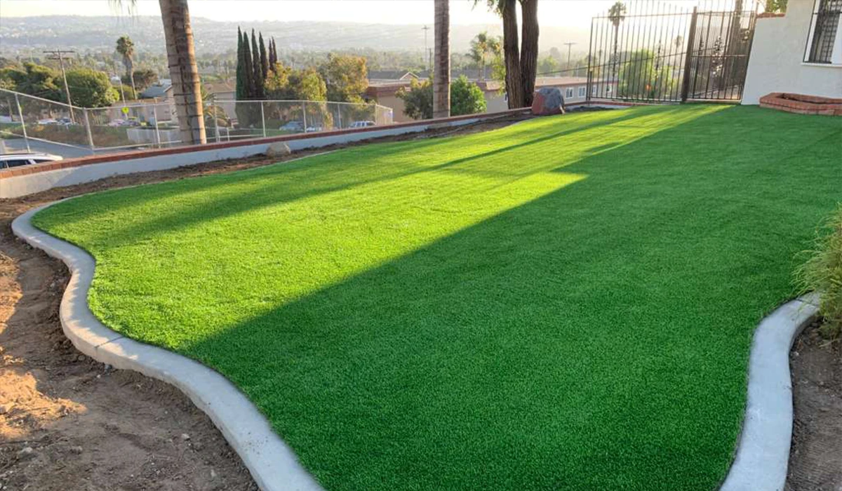 Green artificial grass lawn bordered by concrete, with distant hills in the background