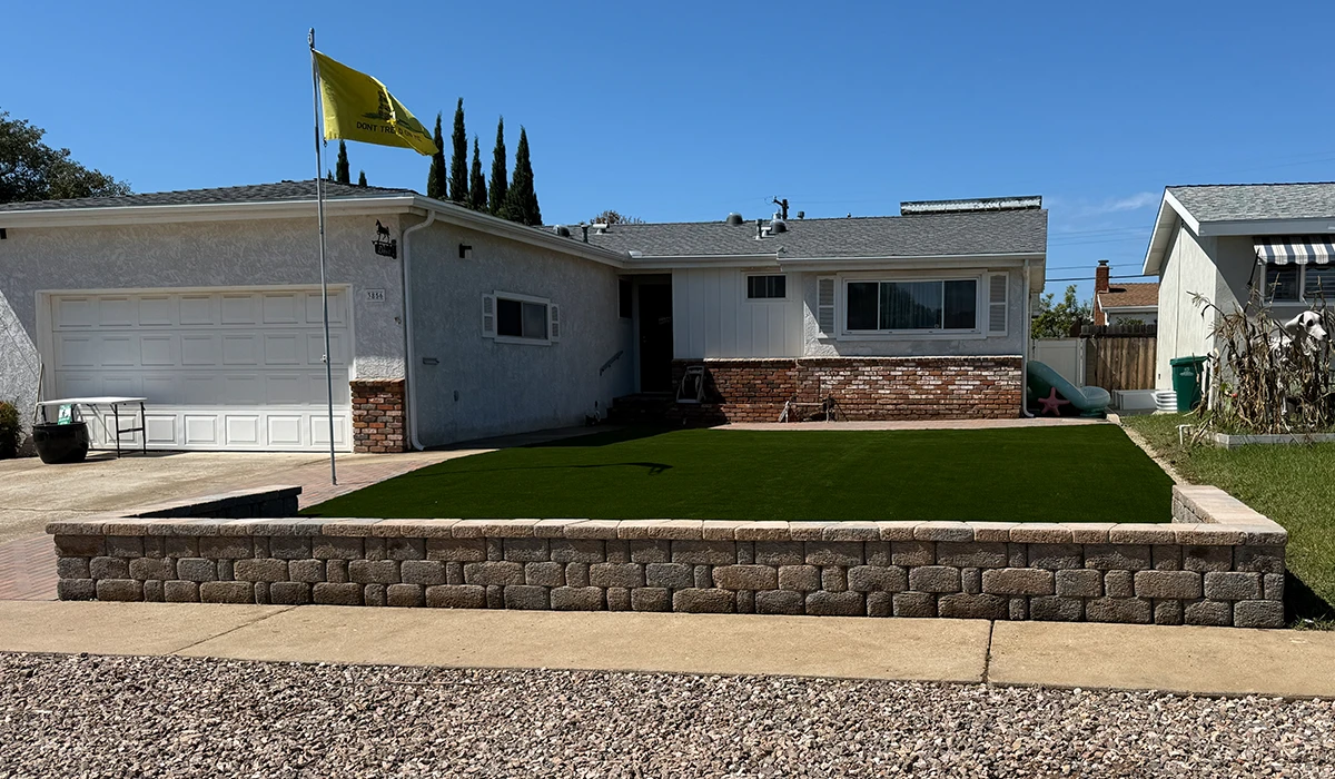 A house with a green lawn, a stone retaining wall, and a yellow flag in front