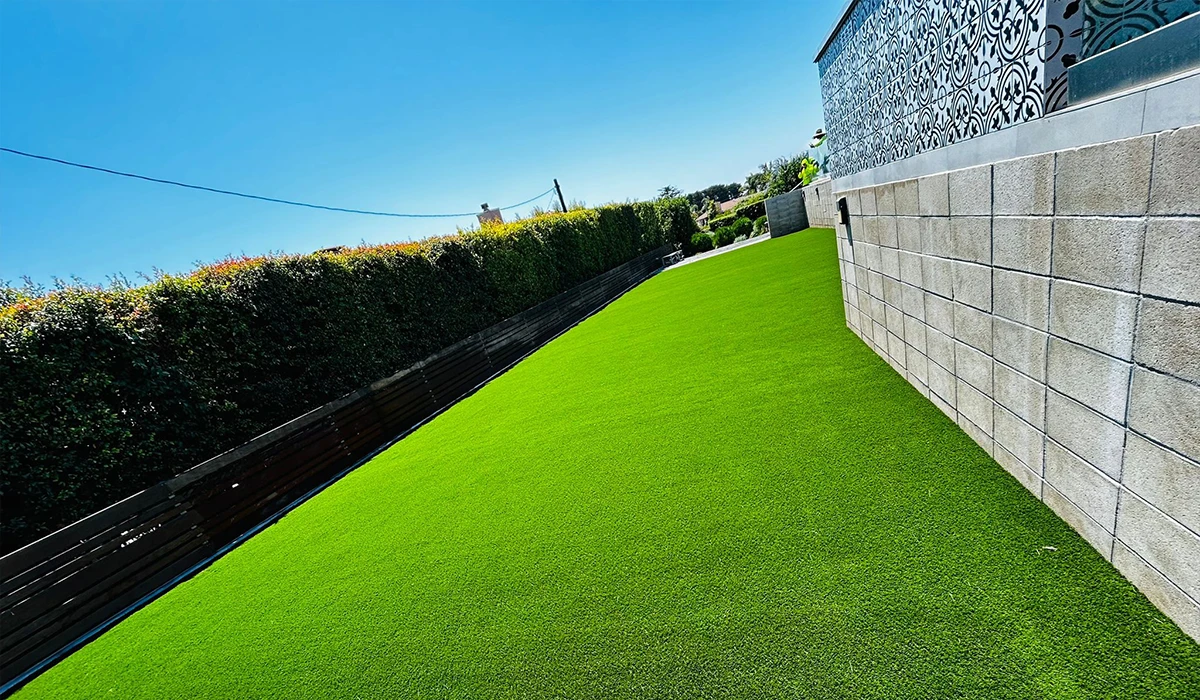 Green artificial grass in a backyard with a stone wall on one side and hedges on the other