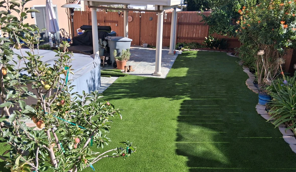 Lawn area with artificial grass, surrounded by plants and a pergola in the background