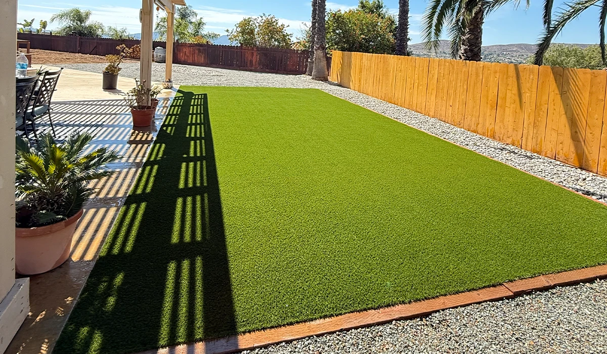 Green artificial grass area with a gravel border and palm trees in the background