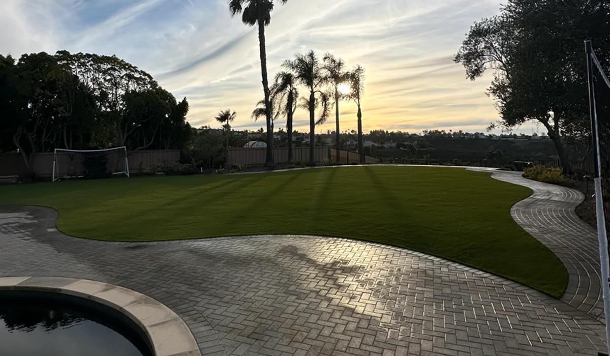 A landscaped lawn with palm trees, stone pathway, and a sunset sky