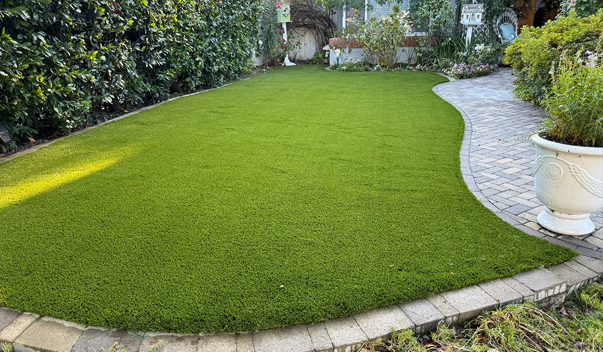 Green artificial grass lawn with a curved stone pathway and planted borders