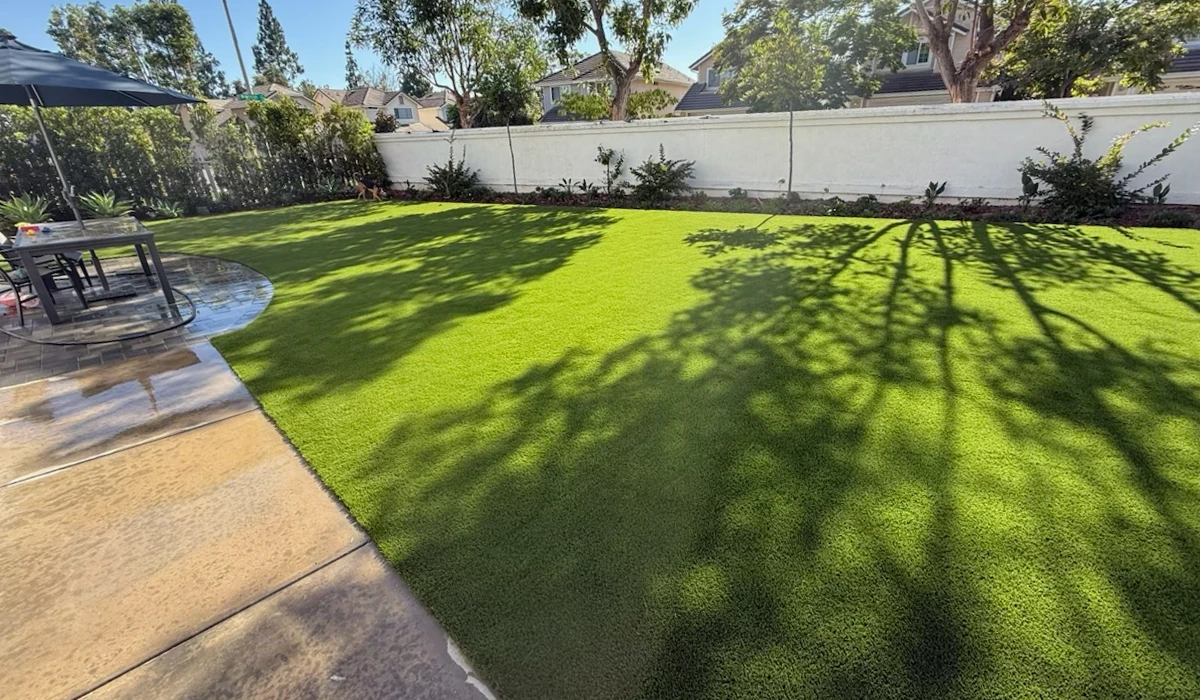 Green lawn with shadows, patio area, and plants along a white fence